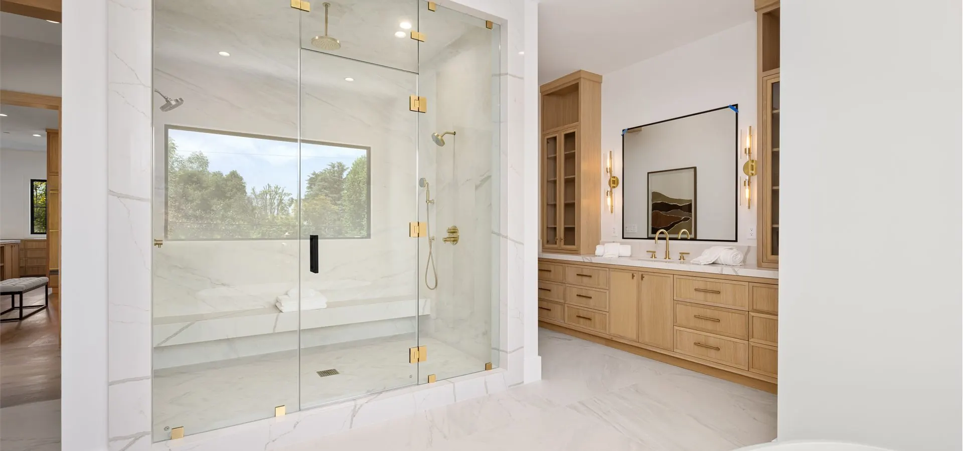 Luxury bathroom remodel in Tacoma WA with large walk-in tile shower, frameless glass, gold fixtures, bench seat, and natural wood double vanity.