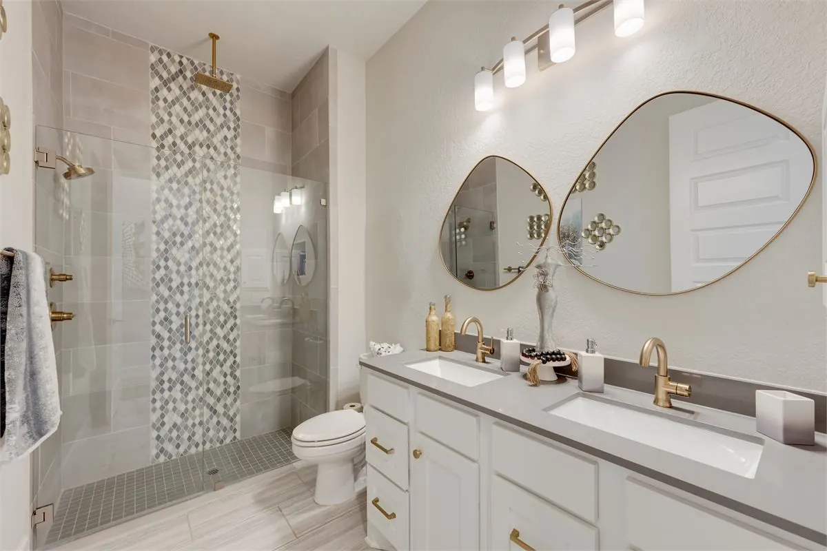 Tub to shower conversion in Tacoma WA with frameless glass shower, gray tile, mosaic accent strip, brass fixtures, and double vanity