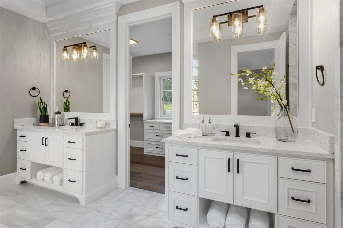 Bathroom vanity remodel in Tacoma WA with white cabinets, black fixtures, stone countertops, large mirrors, and marble-look floor tile